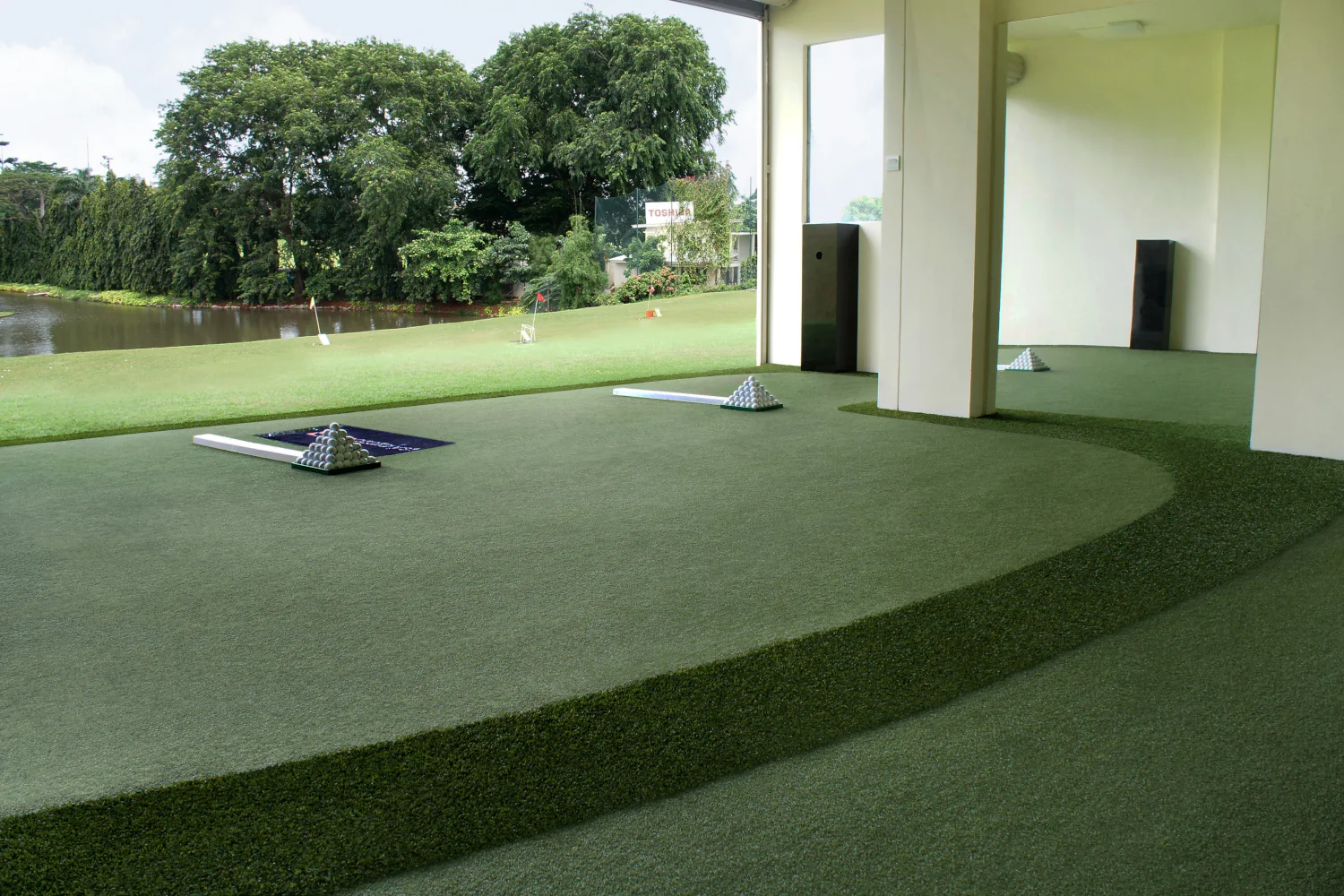 Driving range with artificial turf tee lines with lined-up golf balls on hitting mats set within lush landscaping